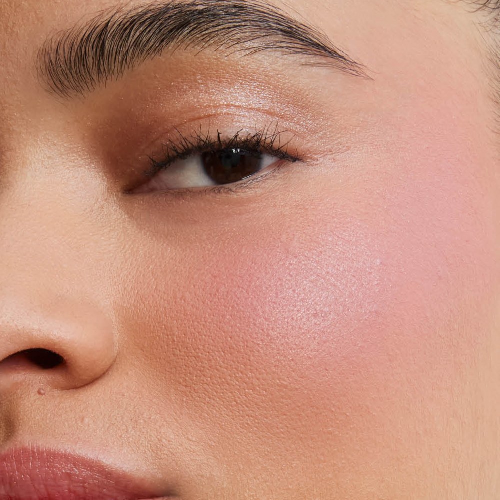 Close-up of a model's cheek showcasing the soft-focus, airbrushed matte finish of Make Me Blush Powder in shade #44 for a buildable, blurred color flush.