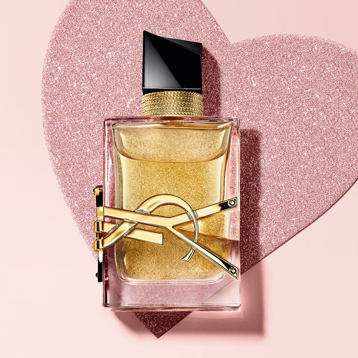 YSL Libre Eau de Parfum, a gold-toned bottle with the YSL logo, on a glittery heart background.