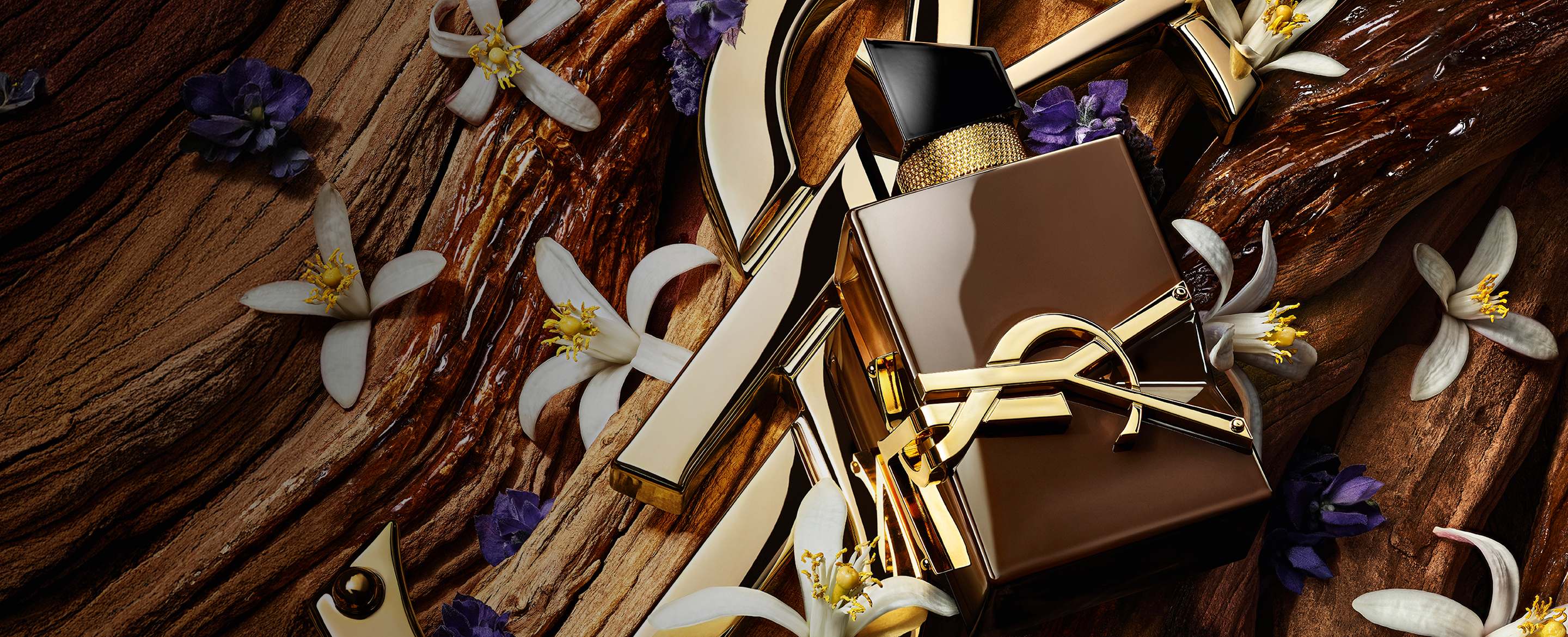 Glazed brown Libre Santal Couture bottle reflecting light, placed on a large golden YSL Cassandre.