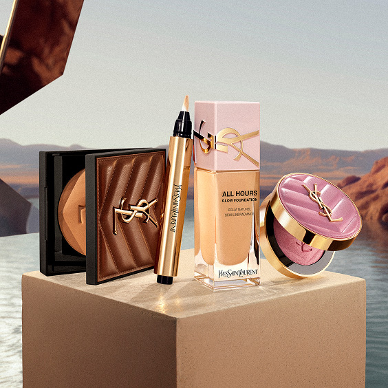 All Hours Hyper Bronze Powder, All Hours Glow Foundation, Touche Éclat le Stylo, and Make Me Blush Powder on a pedestal.