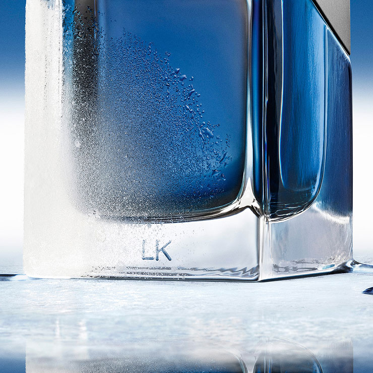 Close-up of the frosted base of a YSL Y Eau de Toilette Intense Iced Cologne bottle, with "LK" engraving, on a cool blue surface.
