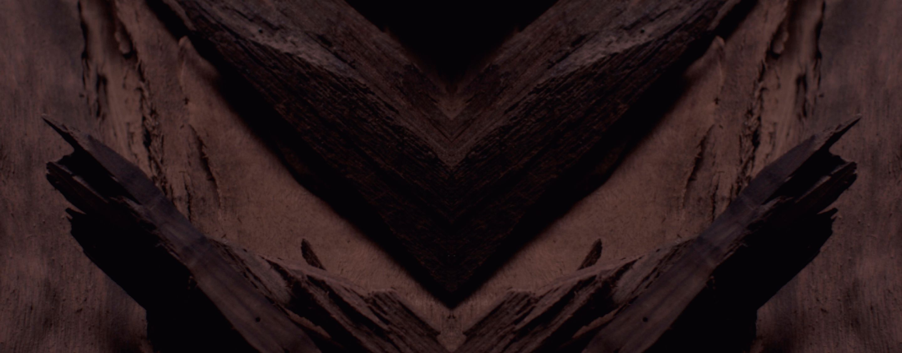 Dark, textured background with a prominent chevron pattern in
deep browns and blacks, designed for YSL LVP Extrait de Parfum
product display.