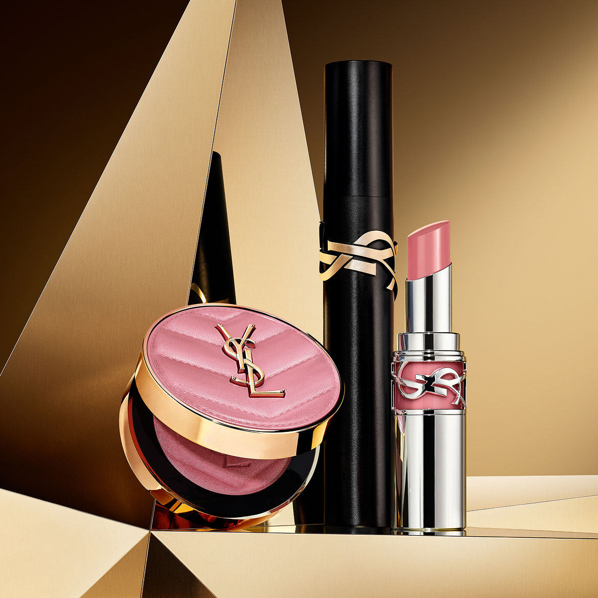 Make Me Blush powder in shade 44, Lash Clash mascara, and YSL Loveshine in shade 44, on a golden geometric background.