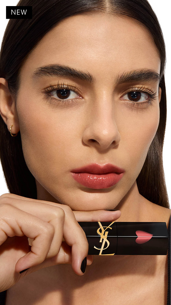 Medium skin tone model posing with the YSL THE INKS VINYL CREAM lip stain held horizontally under her chin, showing a warm, glossy rose lip shade.