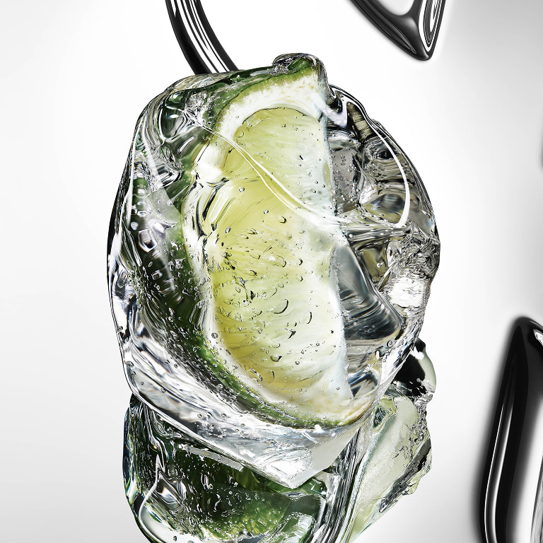 Fresh green bergamot fruit cut in half with water droplets on a reflective YSL Cassandre
background.