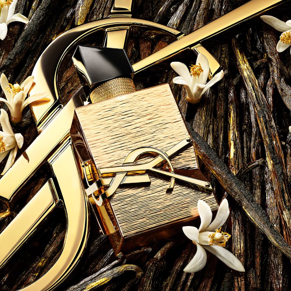 Libre Vanille Couture bottle with gold accents, surrounded by vanilla flowers and rhum accord on a textured background.