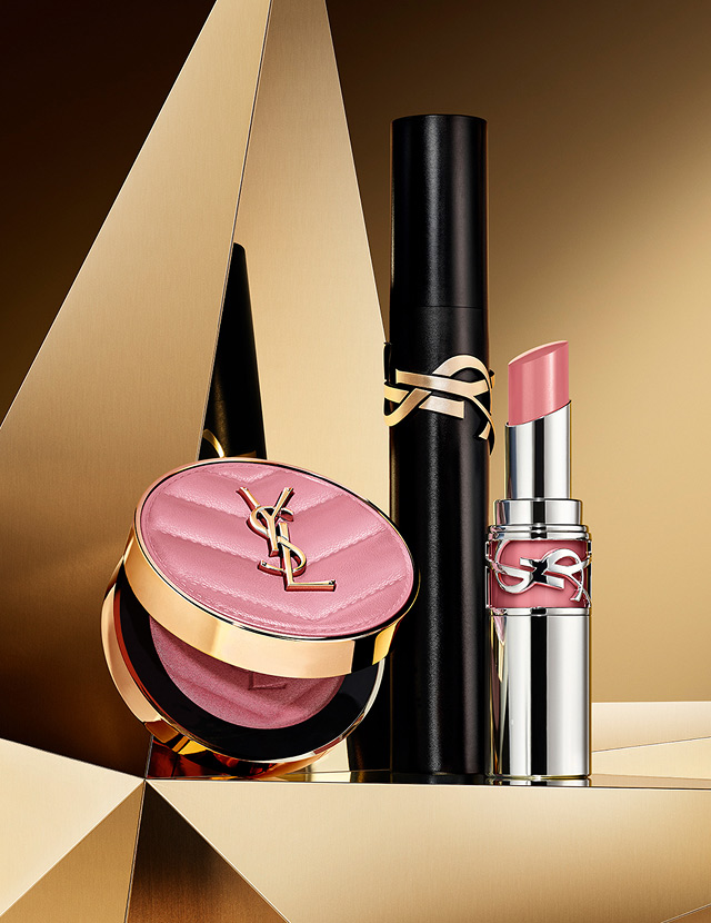 Make Me Blush powder in shade 44, Lash Clash mascara, and YSL Loveshine in shade 44, on a golden geometric background.