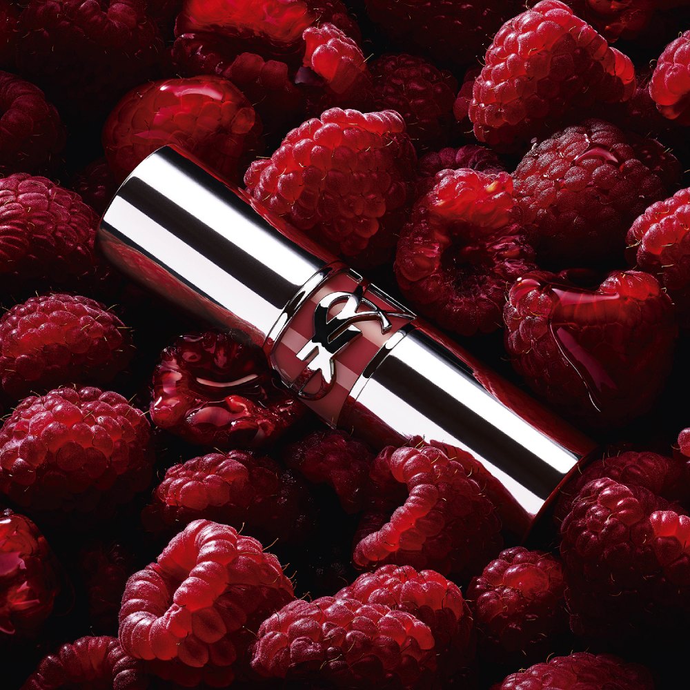 YSL LOVESHINE Berry Crush lipstick, silver tube with berry YSL logo, nestled among fresh raspberries.