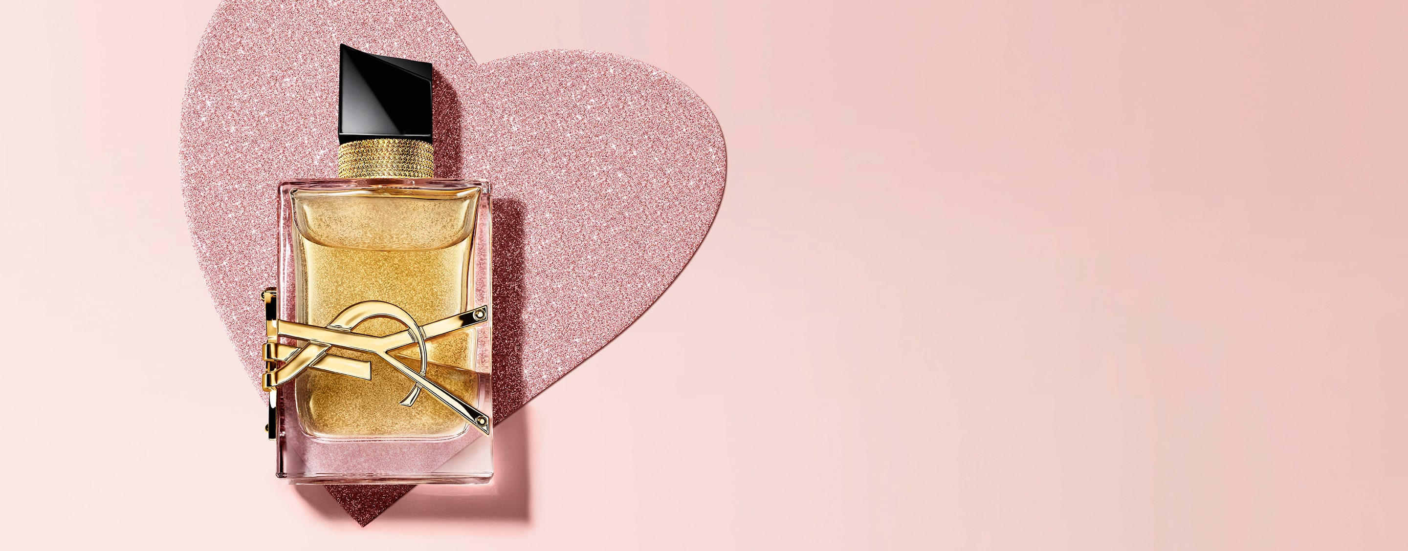 YSL Libre Eau de Parfum, a gold-toned bottle with
the YSL logo, on a glittery heart background.