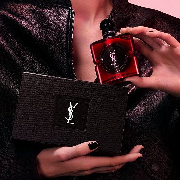 Women's model holding a deep red Black Opium Eau de Parfum Over Red bottle and a black YSL gift box.