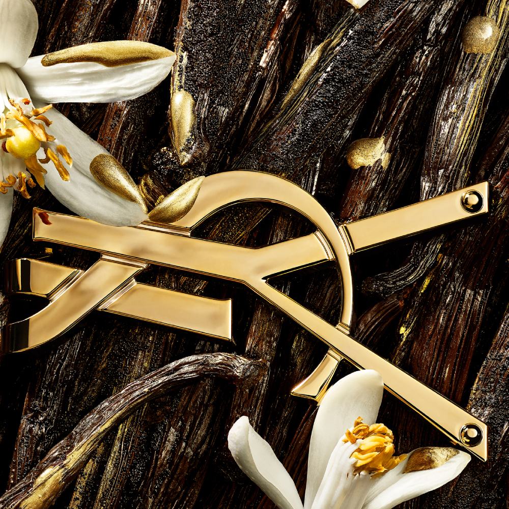 YSL Beauty logo in gold, surrounded by vanilla pods and orange blossom flowers with golden accents.