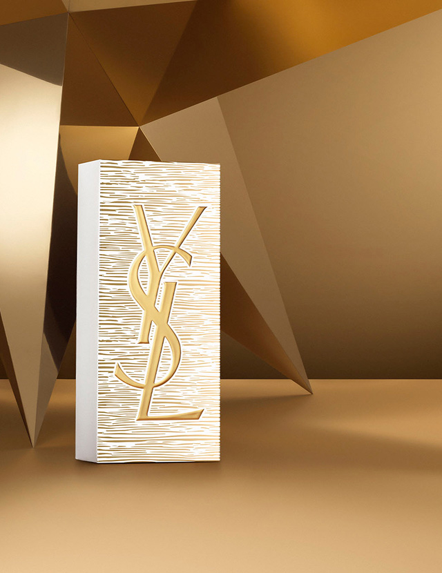 YSL Beauty Holiday gift set box in gold and white, featuring the YSL Beauty logo, on a golden geometric background.