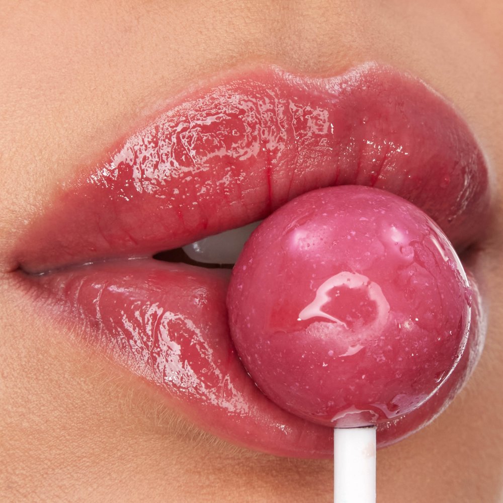 Close-up glossy lips with YSL LOVESHINE CANDY GLOW lip balm and pink candy lollipop.